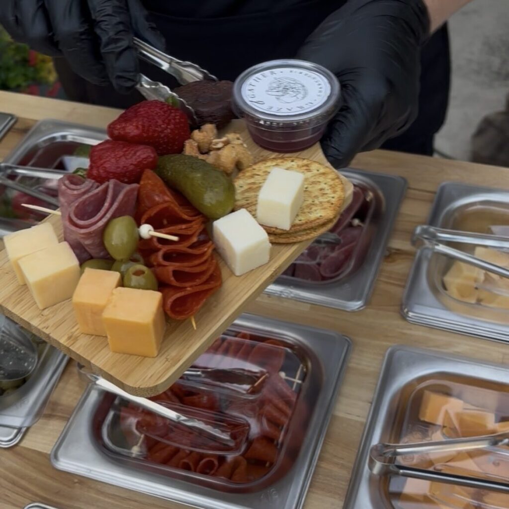 A small wooden cutting board full of meats, cheeses, and accompaniaments over a bar full of food